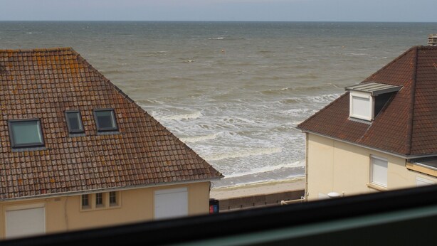 Vista al mar desde una ventana con vista a un edificio de techo a ladrillo.