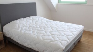 Una cama bien hecha en una habitación con techo inclinado y ventana.