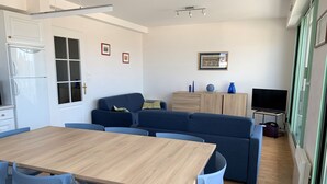 Una sala de estar moderna con una mesa de comedor de madera, sillas azules, un sofá azul y un televisor sobre un mueble.
