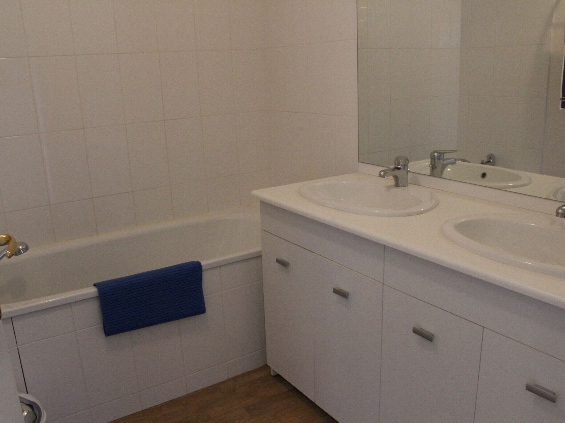 Casa de banho com banheira, duas pias, um espelho e uma toalha azul na parede.