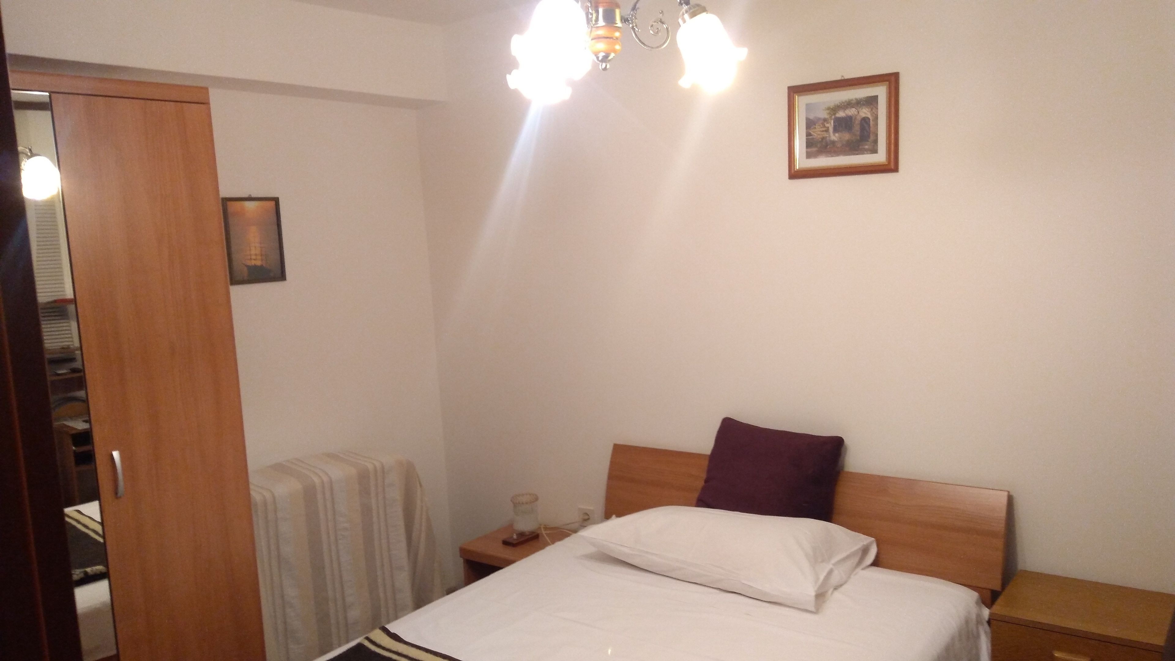 A bedroom with a bed, a nightstand, a bedside table, a lamp, a picture on the wall, and a door.