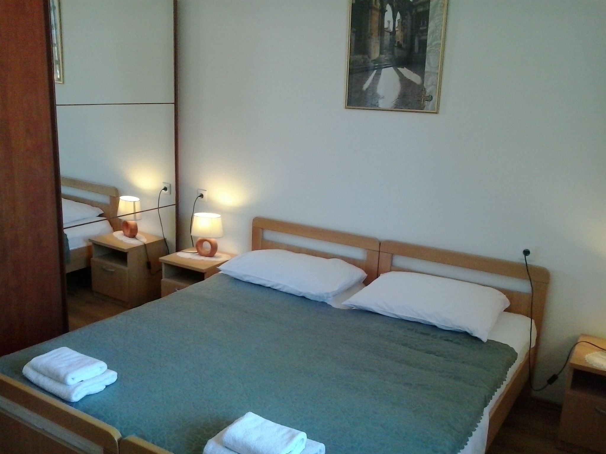 Une chambre d’hôtel avec un lit, deux tables de chevet avec des lampes, un miroir et un tableau au mur.
