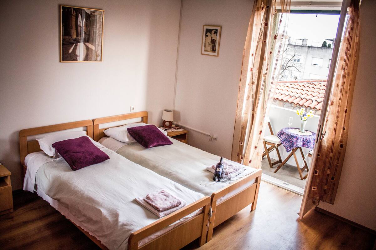 A double bed with two pillows, a small bedside table, and a window with curtains.