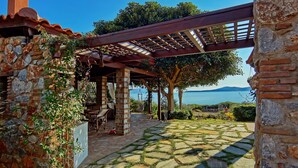 A stone building with a pergola over a patio area, a view of the sea, and a stone pathway.