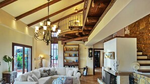 A spacious living room with a white sofa, a wooden coffee table, and a fireplace. There is a staircase with a wooden railing leading to an upper level.