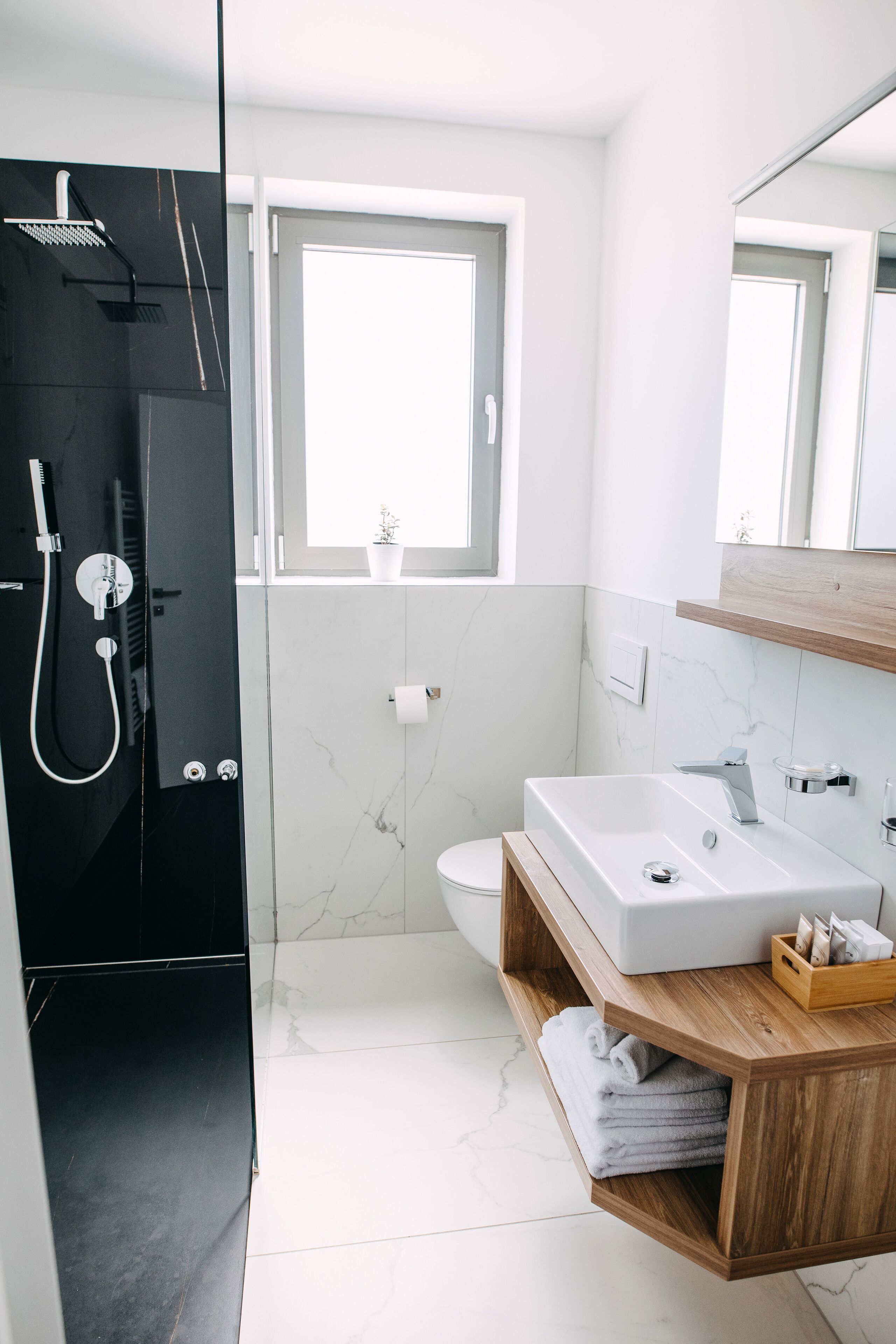 A modern bathroom with a black shower enclosure, a white sink, and a wooden vanity.