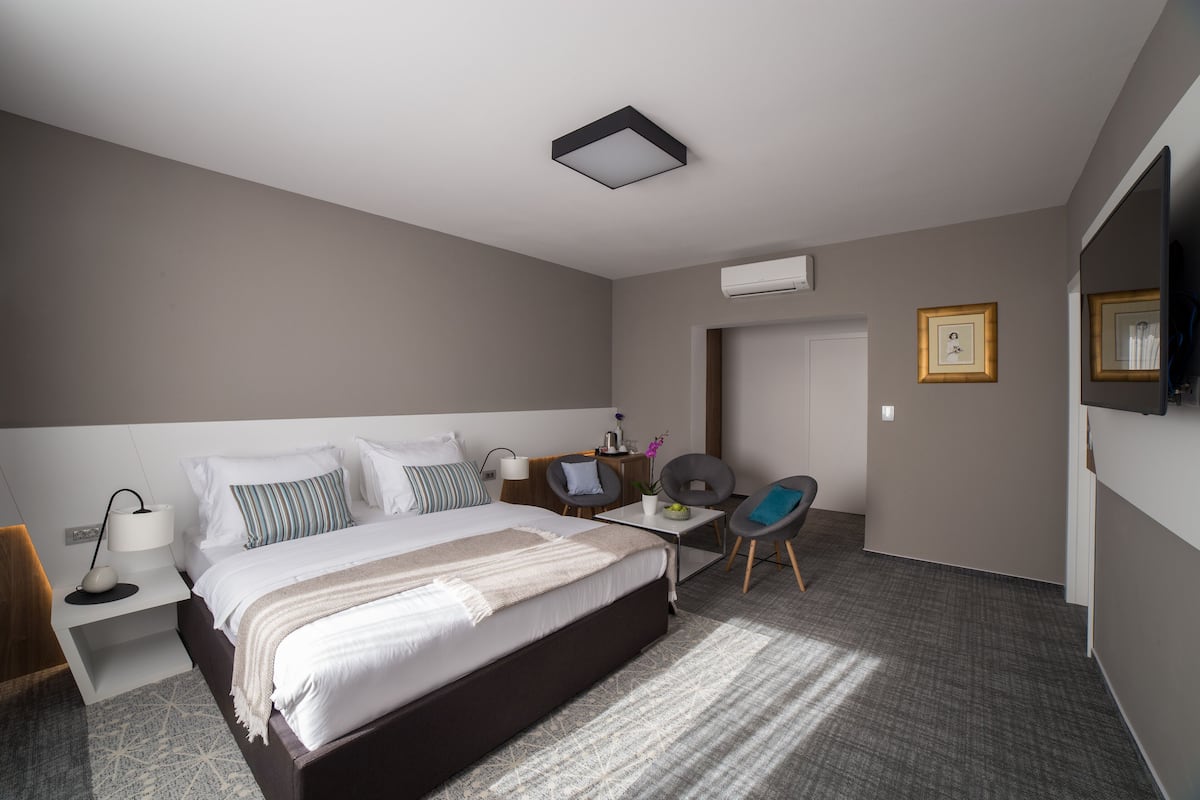 A modern hotel room with a large bed, a desk, a chair, a small table, and a TV.