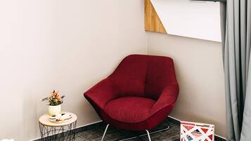 Una habitación de hotel moderna con un sillón rojo, una mesita redonda con un jarrón de flores y un televisor de pantalla plana montado en la pared.