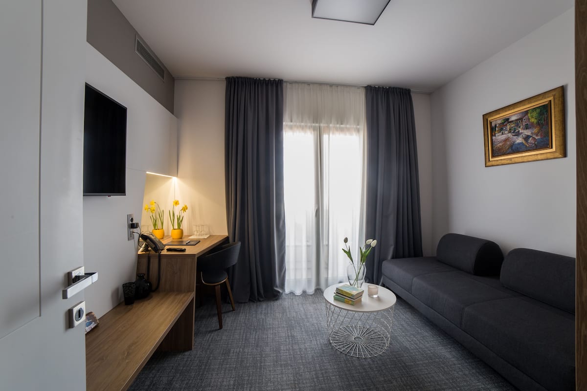 A modern hotel room with a desk, a sofa, a round coffee table, and a painting on the wall.