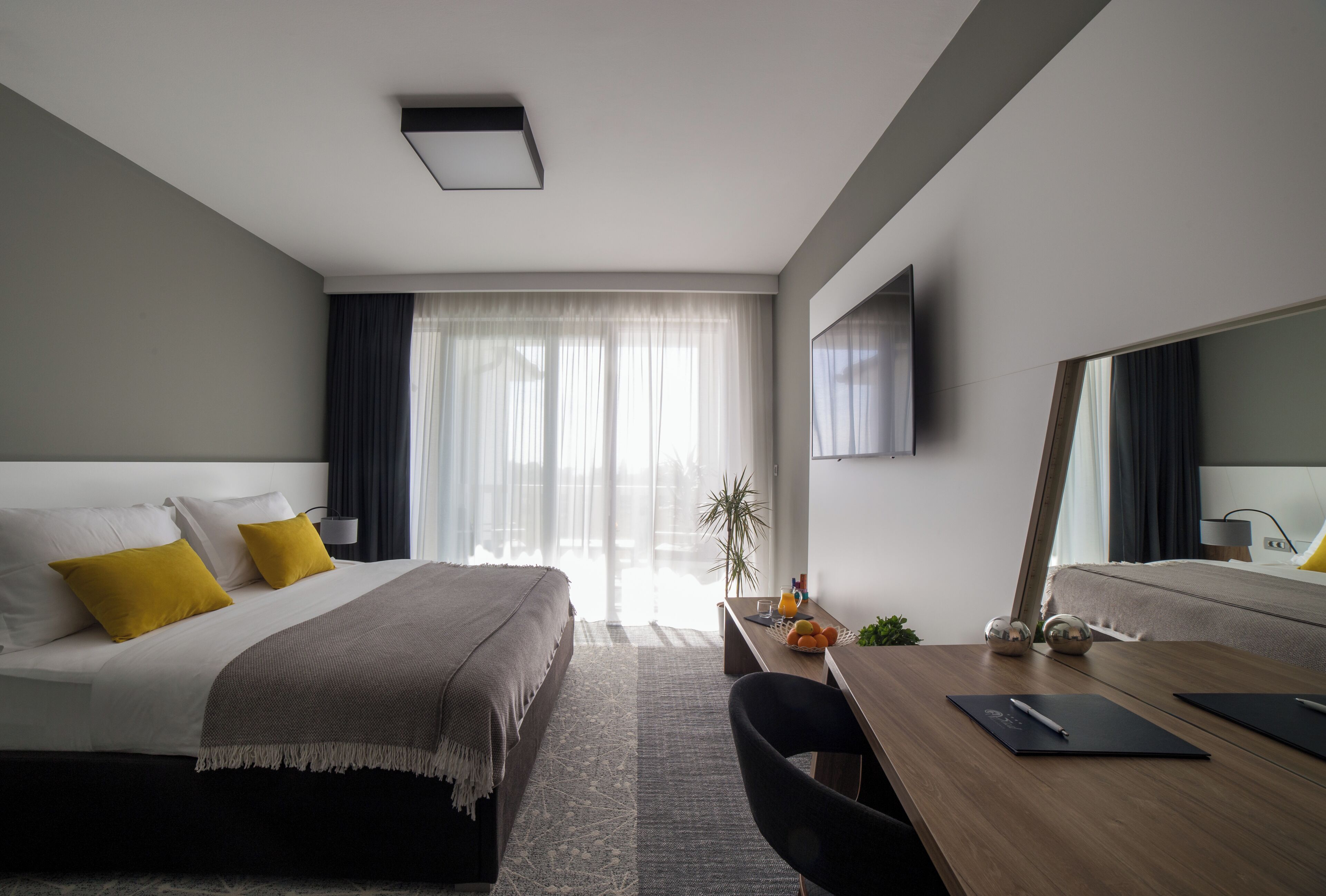 Quarto de hotel moderno com cama, escrivaninha, cadeira e um espelho grande.