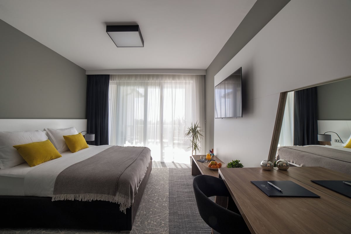 A modern hotel room with a bed, desk, chair, and a large mirror.