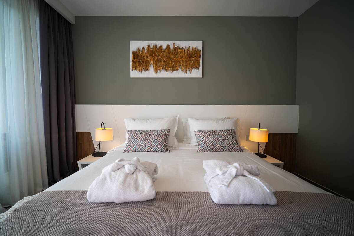 A hotel room with a large bed, two bedside lamps, patterned pillows, and a wall art piece.
