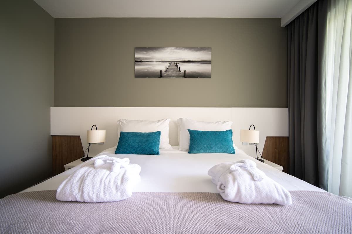 A hotel room with a large bed, two pillows, two bedside lamps, and a painting on the wall.