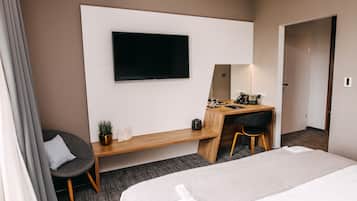 A hotel room with a bed, a desk with a chair, a television, and a small potted plant.