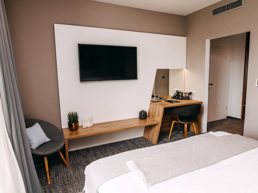 A hotel room with a bed, a desk with a chair, a television, and a small potted plant.