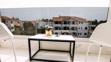 A balcony with a white table and chairs, a vase with flowers, and a view of buildings.