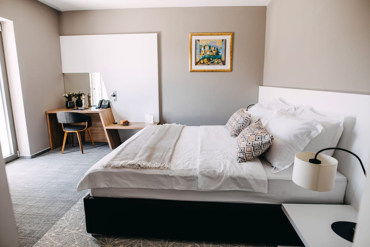 A modern bedroom with a bed, bedside table, lamp, desk, chair, and a painting on the wall.