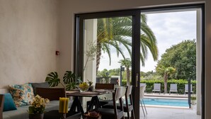 Un soggiorno moderno con angolo pranzo, ampie finestre e vista su una piscina e vegetazione.