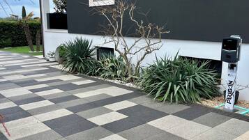Un edificio moderno con pavimento de baldosas a cuadros, un pequeño árbol y una estación de carga con la etiqueta 'Plug In'.