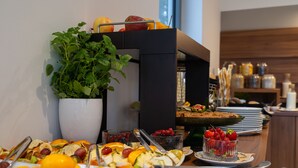 Un buffet con diversi tipi di frutta, una pianta in vaso e una pila di piatti.