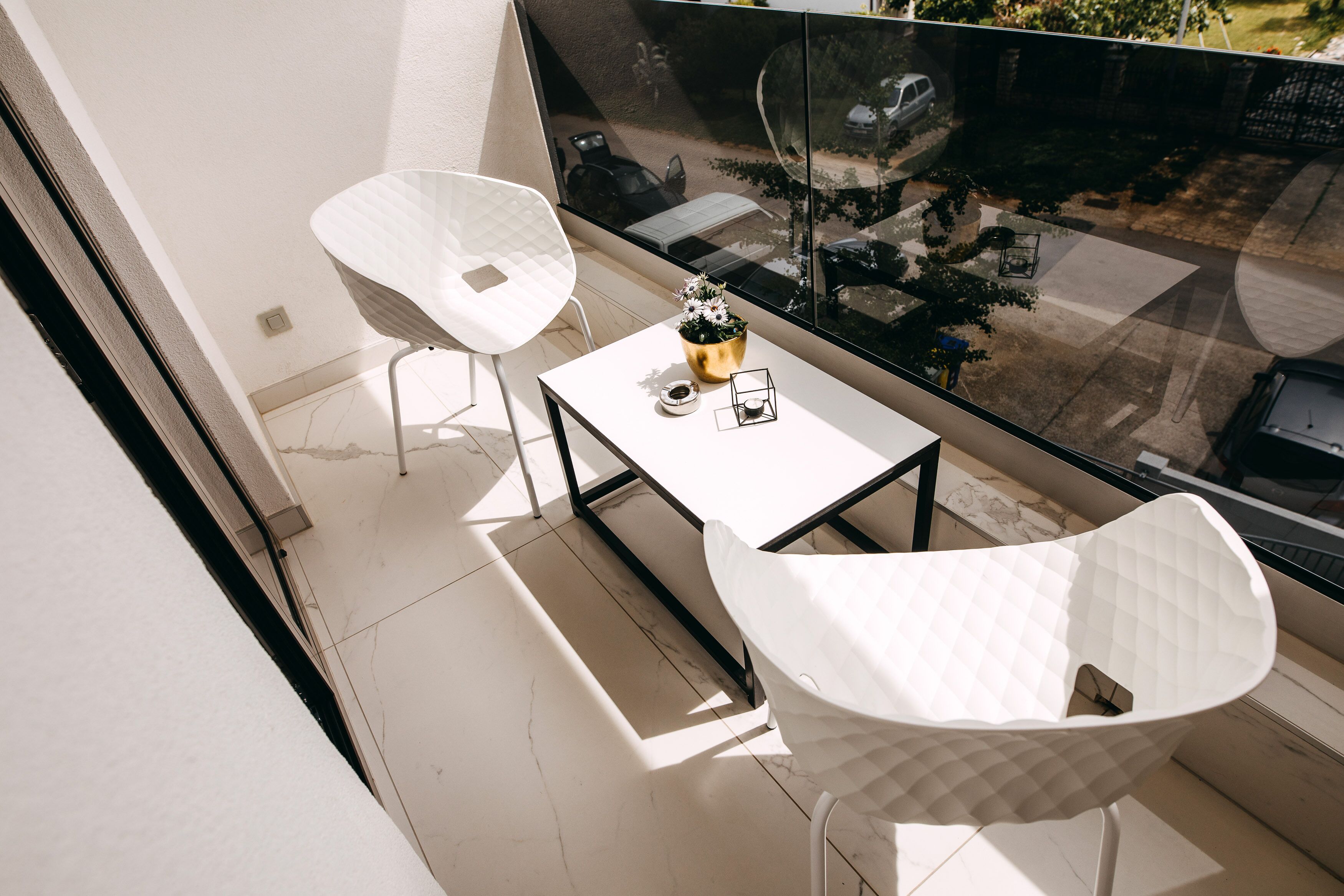 A balcony with two white chairs, a small table, and a potted plant.