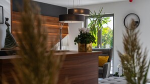 Un soggiorno moderno con una scrivania in legno per la reception, una lampada da terra grande e un divano con un cuscino giallo.