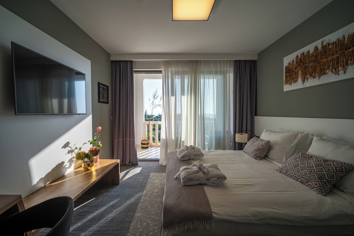 A modern hotel room with a large bed, a desk, a flat-screen TV, and a balcony with curtains.