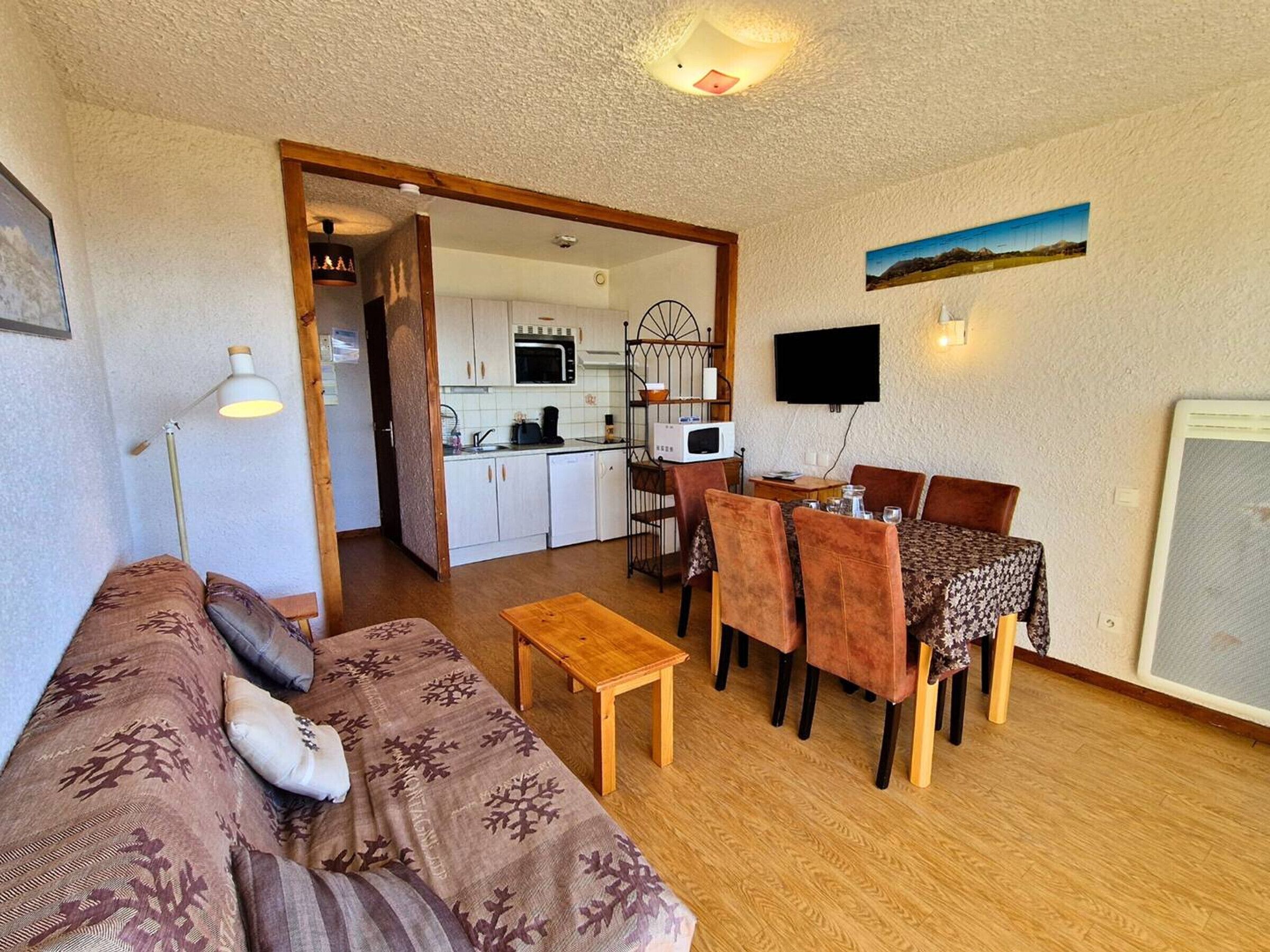 Un espacio habitable compacto con sofá, mesa de comedor, sillas, una pequeña cocina y un televisor.