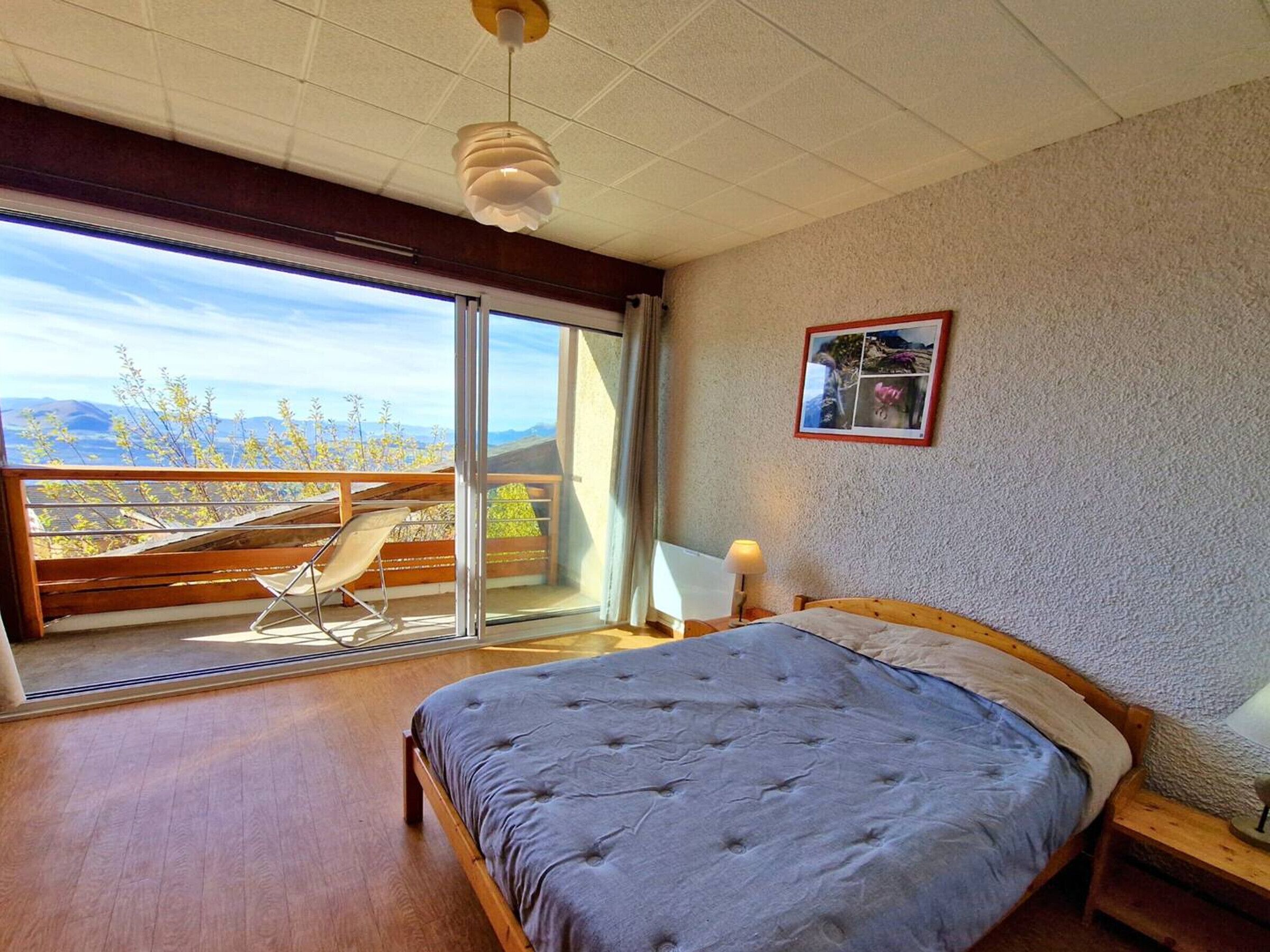 A bedroom with a large bed, a wooden nightstand, a bedside lamp, a window with a view of the outdoors, and a ceiling fan.