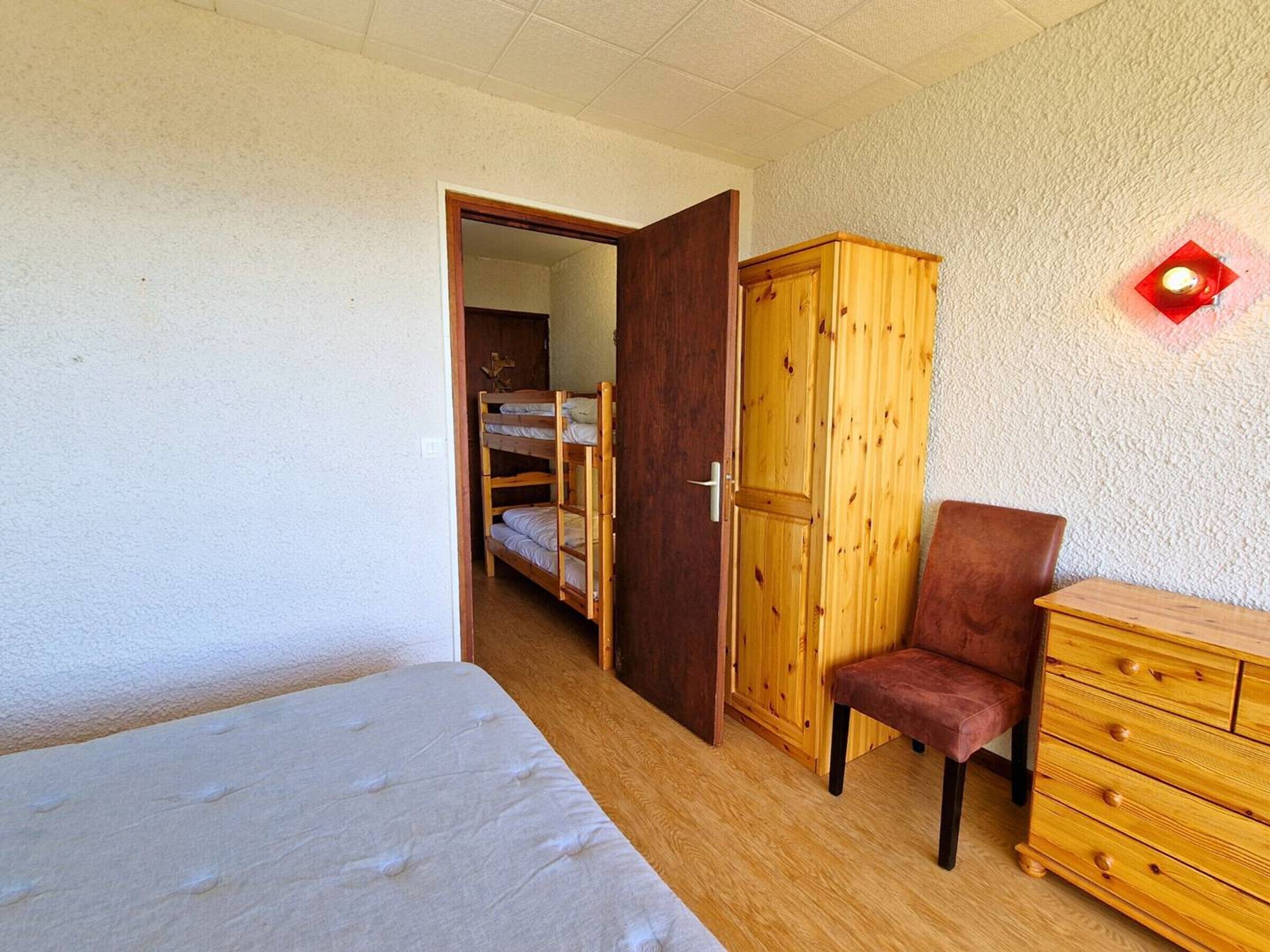 A bedroom with a bunk bed, wooden wardrobe, a chair, and a dresser.