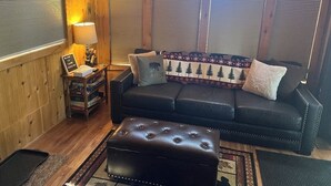 Ein gemütliches Wohnzimmer mit einer schwarzen Ledersofa, passendem Hocker und einem gemusterten Tagesdecken.