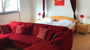A bedroom with a bed, a red sofa, a ceiling fan, a window, and a red curtain. - City Hotel Kaiserhof (Saarbrücken)