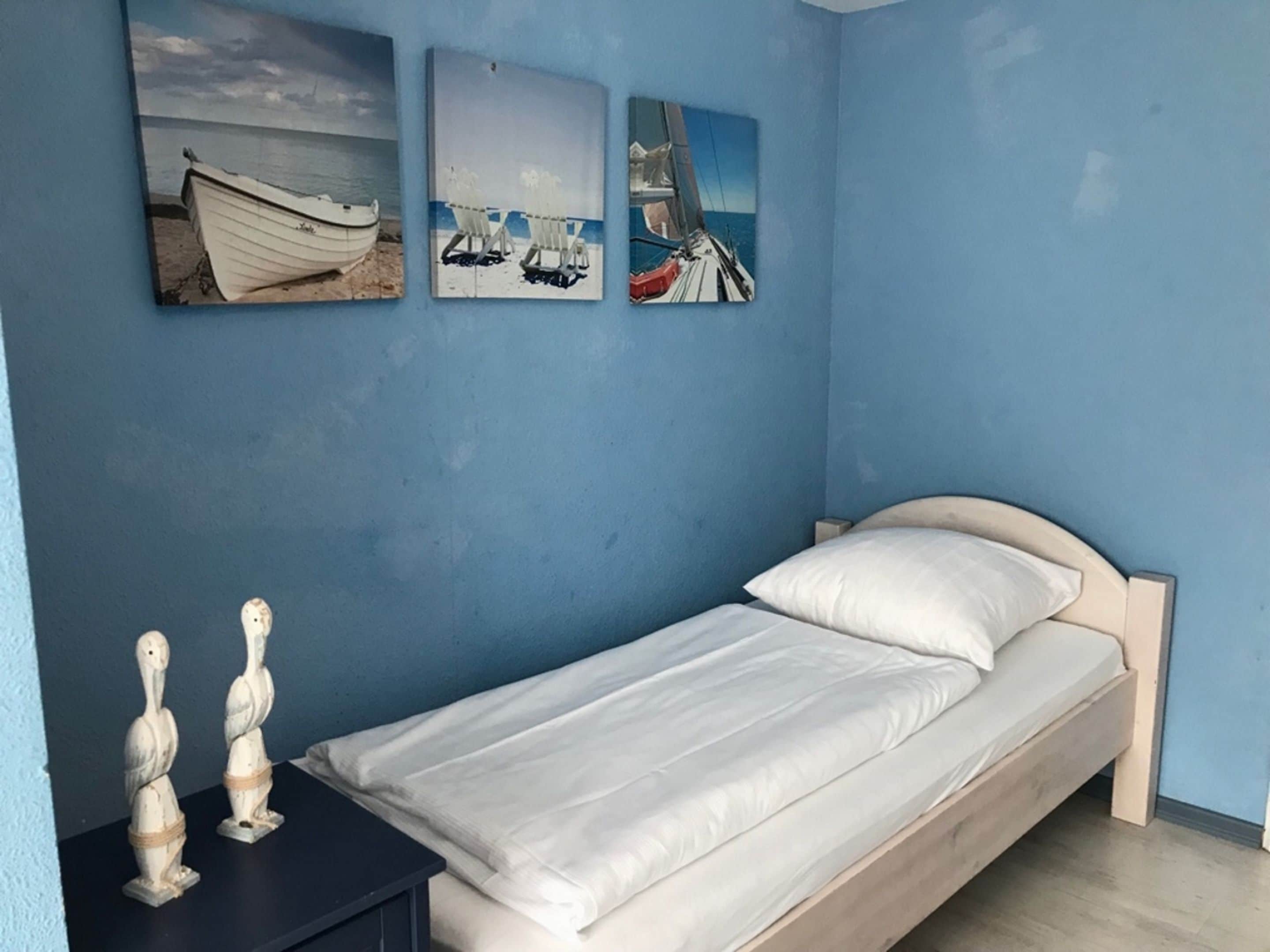 A bedroom with a single bed, a nightstand, and three wall-mounted pictures depicting boats and sailing scenes.