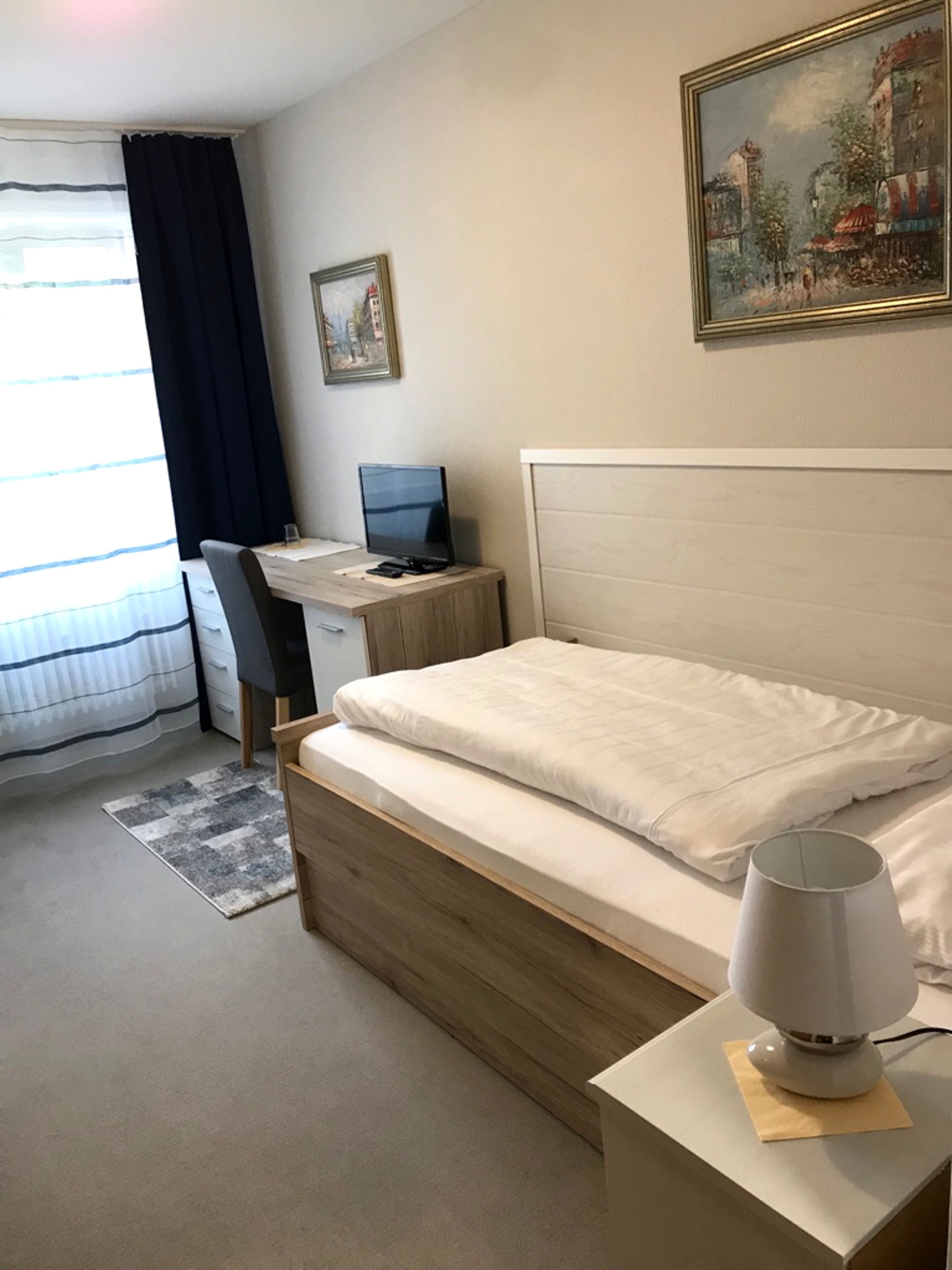 Una habitación de hotel con cama, escritorio, computadora y lámpara.