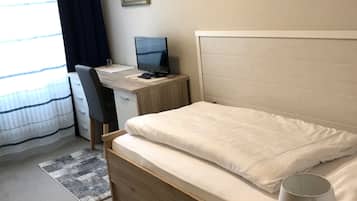 Una habitación de hotel con cama, escritorio, computadora y lámpara.