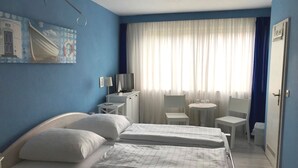 A hotel room with two beds, a desk with a TV, a chair, and a small table. - City Hotel Kaiserhof (Saarbrücken)