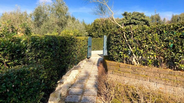 A pathway leading to a gated entrance surrounded by dense foliage and a clear blue sky. - N198 - Numana, new three-room apartment with garden and swimming pool (Sirolo)