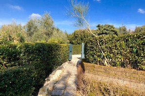 A pathway leading to a gated entrance surrounded by dense foliage and a clear blue sky.