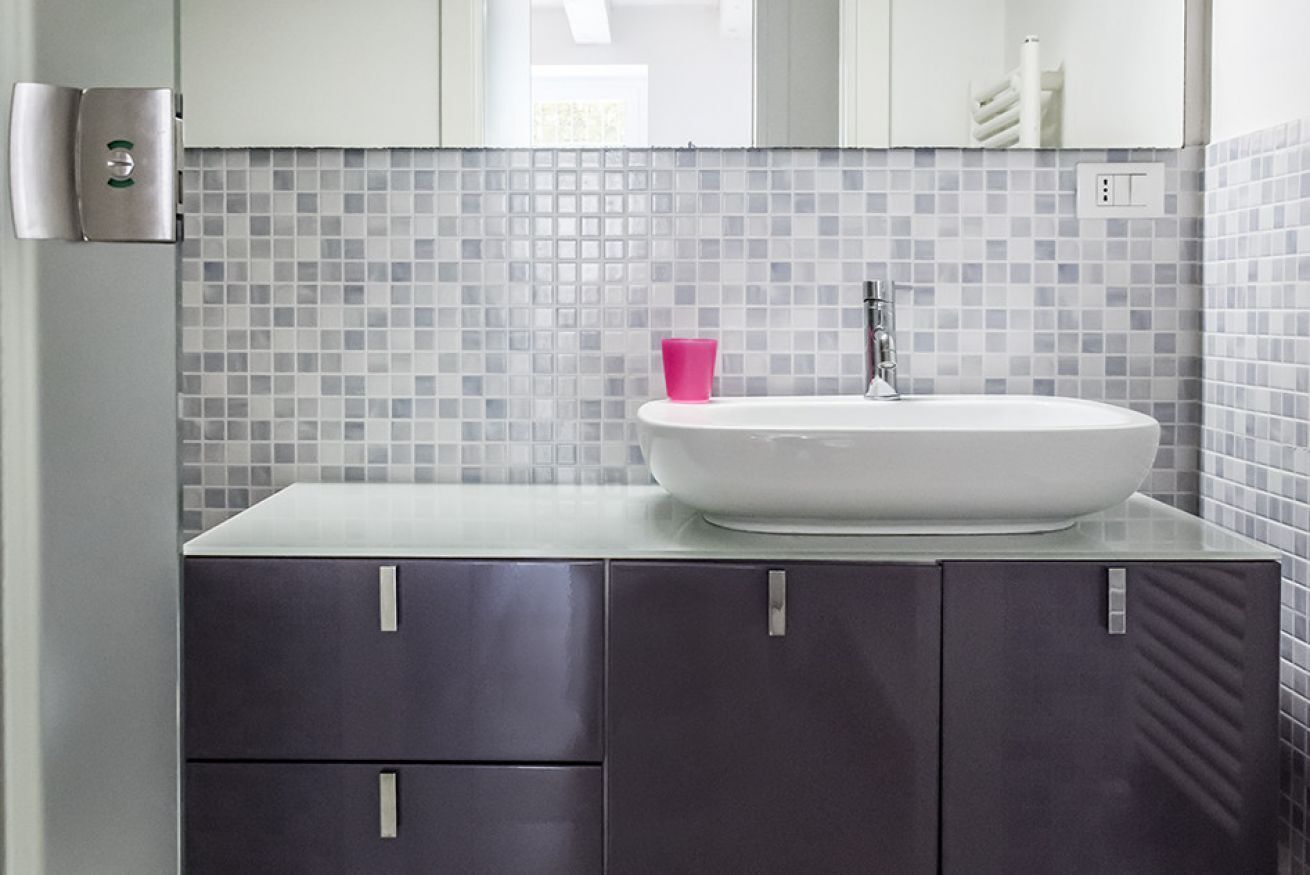 Een badkamer met een witte wastafel, een roze beker en een betegelde spatwand.