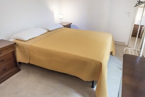 A single bed with a yellow bedspread, a bedside table with a lamp, a wooden dresser, and a mirror on the wall.