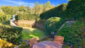 A garden with a wooden table and chairs, surrounded by lush greenery and a stone wall. - N198 - Numana, new three-room apartment with garden and swimming pool (Sirolo)