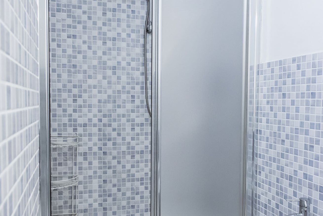 A shower with a tiled wall and a metal rack.