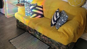 A yellow sofa with patterned cushions, a decorative vase with sunflowers, and a wall clock.