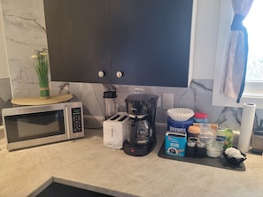 Uma cozinha com micro-ondas, torradeira, cafeteira e diversos utensílios sobre o balcão.