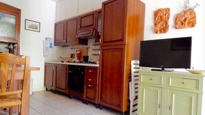 Une cuisine avec des meubles en bois, une cuisinière, un téléviseur et un coin repas avec une chaise.