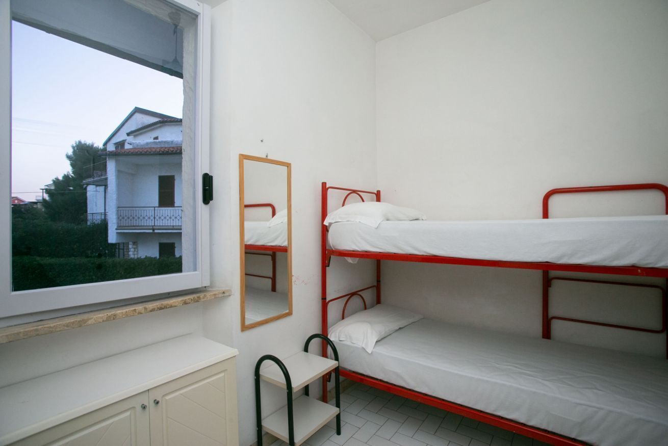 Une chambre avec un lit superposé, une fenêtre, un miroir et une petite table.