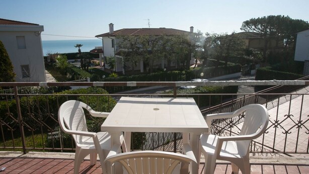 A balcony with a table and chairs, overlooking a residential area with houses and a body of water. - M087 - Marcelli, three-room apartment with terrace at the Mareverde residence (Marcelli)