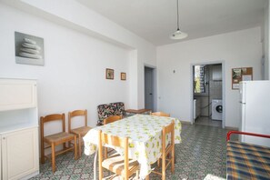 A dining area with a table and chairs, a kitchen in the background, and a patterned floor.