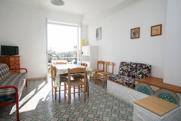 Una habitación con cama, sofá, mesa de comedor con sillas, televisor y refrigerador.