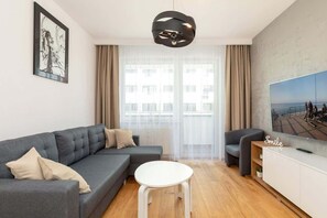 Relax in this stylish living room with a comfortable sofa, coffee table, and armchair, perfect for unwinding in front of the large flat-screen TV.
